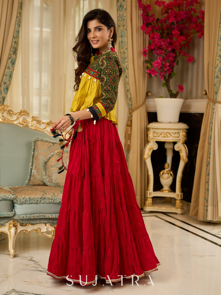 Red tiered Jamdani lehenga with a striking green Ajrakh and mustard jamdani choli featuring intricate mirror work & shell tassels .