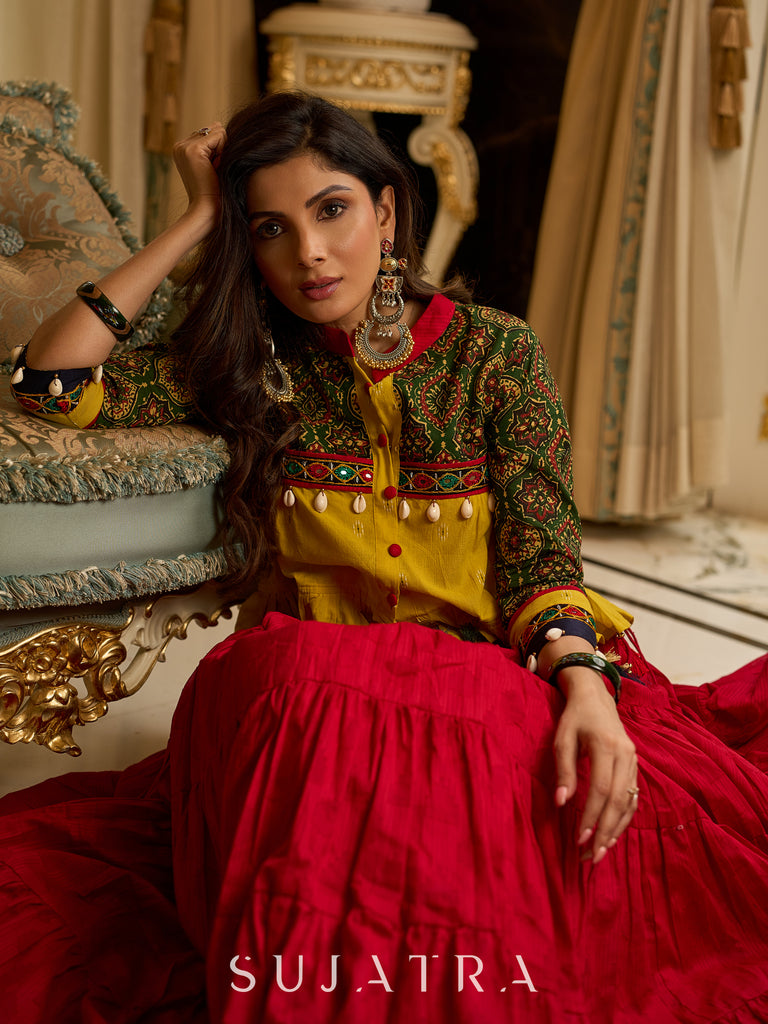 Red tiered Jamdani lehenga with a striking green Ajrakh and mustard jamdani choli featuring intricate mirror work & shell tassels .