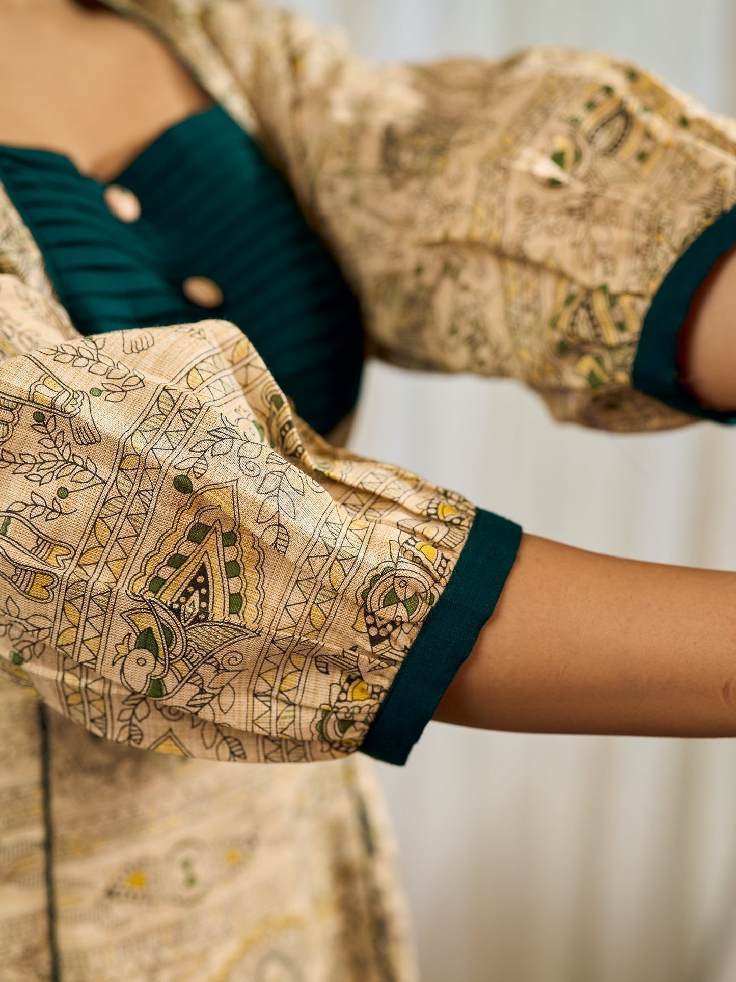 Artisanal beige Madhubani dress featuring intricate motifs, a contrasting green yoke, and refined accents.
