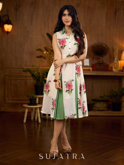 White floral printed sleeveless dress featuring fresh green accents, a structured shirt collar with contrast buttons, and a panelled silhouette with inner green pleats for added flow and movement.