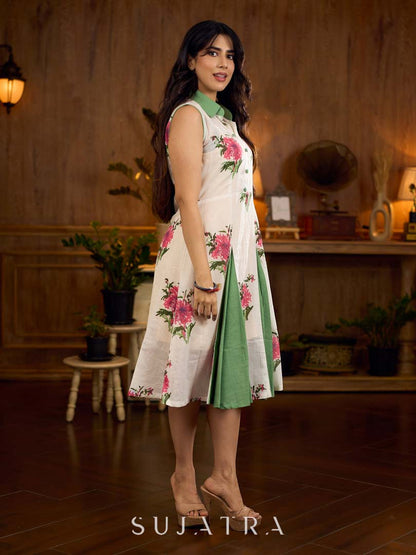 White floral printed sleeveless dress featuring fresh green accents, a structured shirt collar with contrast buttons, and a panelled silhouette with inner green pleats for added flow and movement.