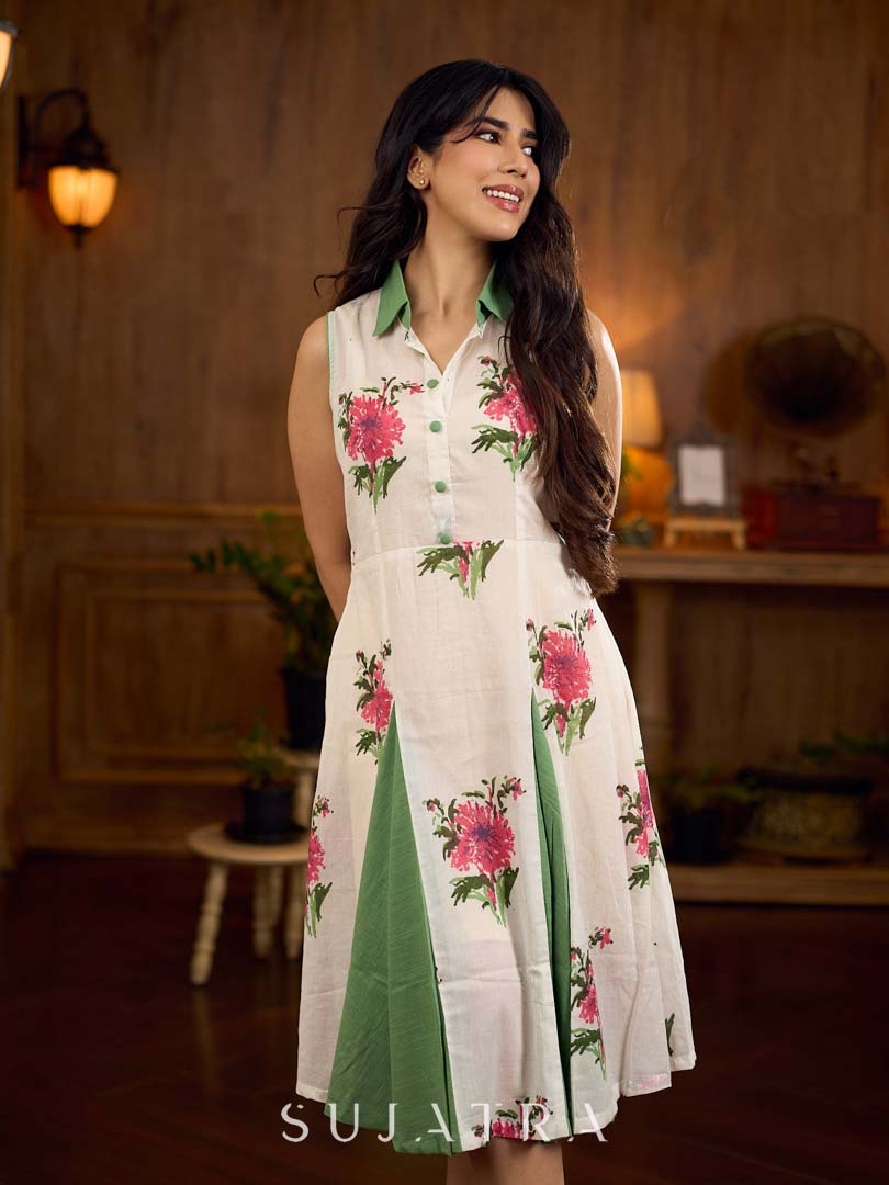 White floral printed sleeveless dress featuring fresh green accents, a structured shirt collar with contrast buttons, and a panelled silhouette with inner green pleats for added flow and movement.