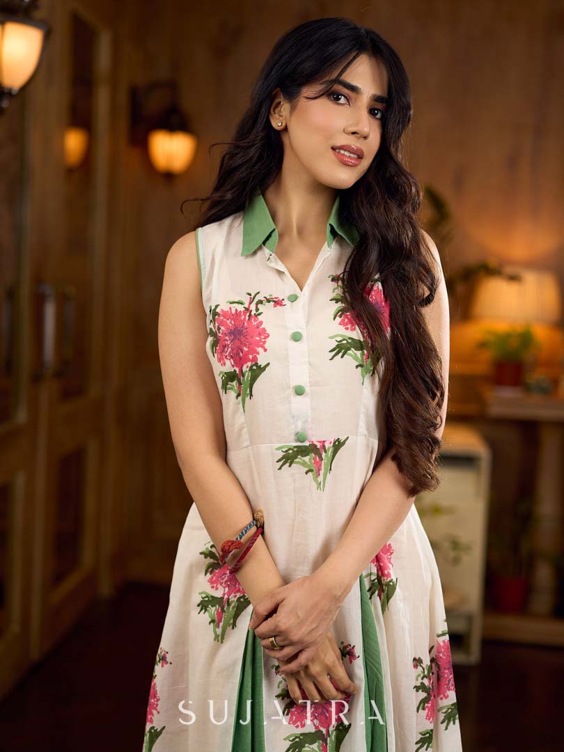White floral printed sleeveless dress featuring fresh green accents, a structured shirt collar with contrast buttons, and a panelled silhouette with inner green pleats for added flow and movement.