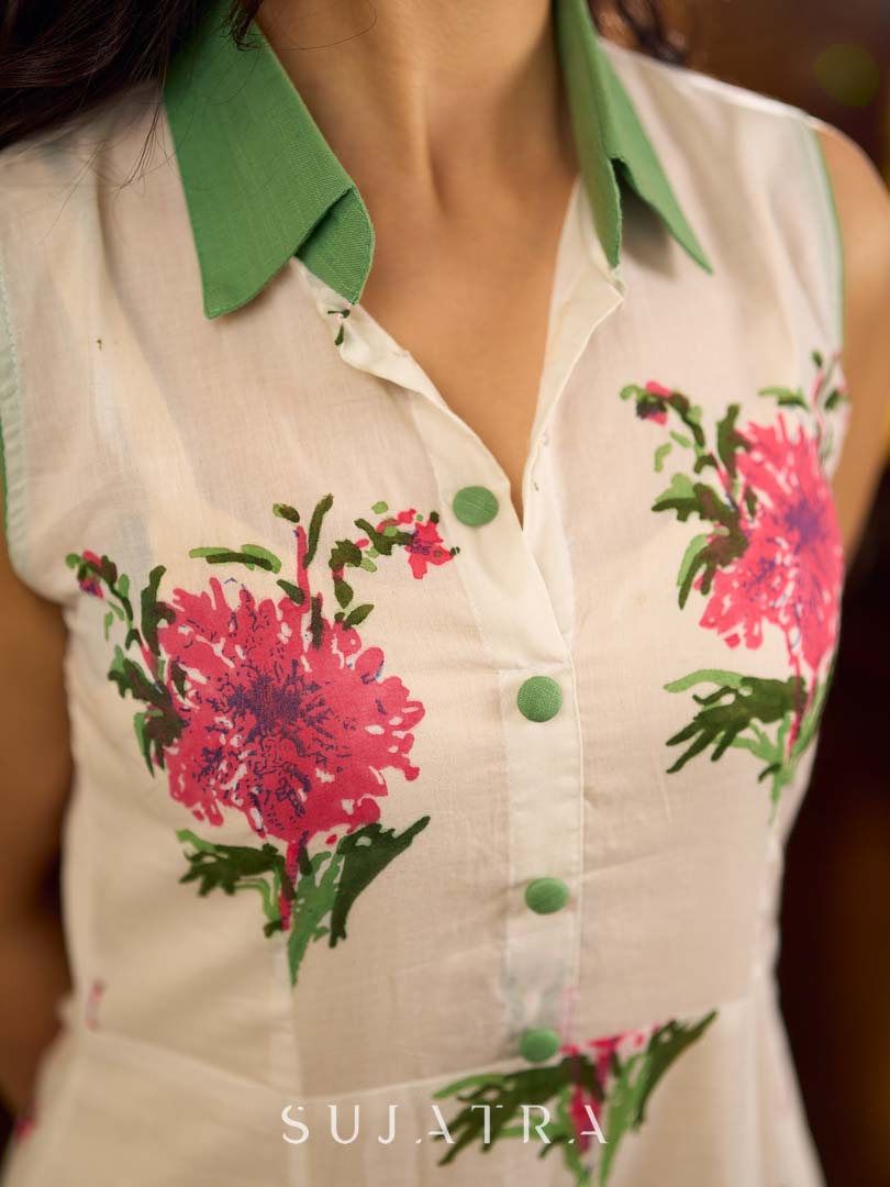 Dussehra Sale — White floral printed sleeveless dress featuring fresh green accents, a structured shirt collar with contrast buttons, and a panelled silhouette with inner green pleats for added flow and movement.