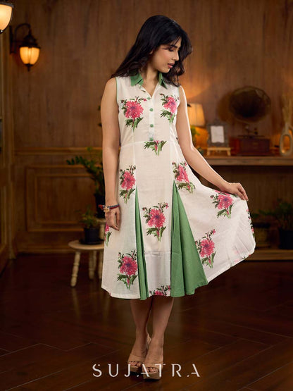 White floral printed sleeveless dress featuring fresh green accents, a structured shirt collar with contrast buttons, and a panelled silhouette with inner green pleats for added flow and movement.