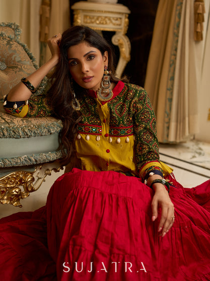 Red tiered Jamdani lehenga with a striking green Ajrakh and mustard jamdani choli featuring intricate mirror work & shell tassels .