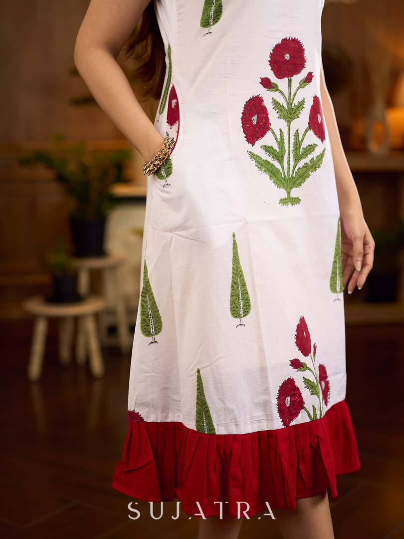 White sleeveless dress featuring red butta motifs and a gathered red panel at the hem, finished with coordinated red accents for a fresh, playful silhouette with a touch of traditional charm.