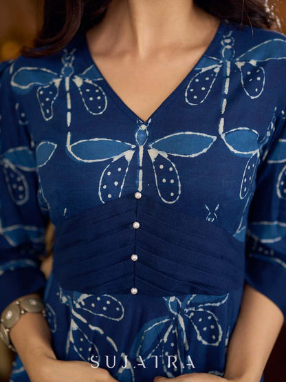 Indigo printed dress featuring dragonfly motifs, gathered sleeves with cuffs, and navy blue pleated waist detailing accented with pearls, creating a graceful silhouette with refined artisanal charm.