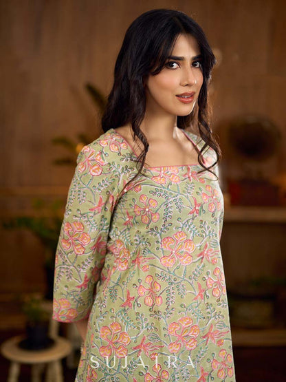 Soft green Gulmohar-printed dress featuring a square neckline and pearl-highlighted motifs, finished with an elasticated waist to create a flattering cinched silhouette with effortless charm.