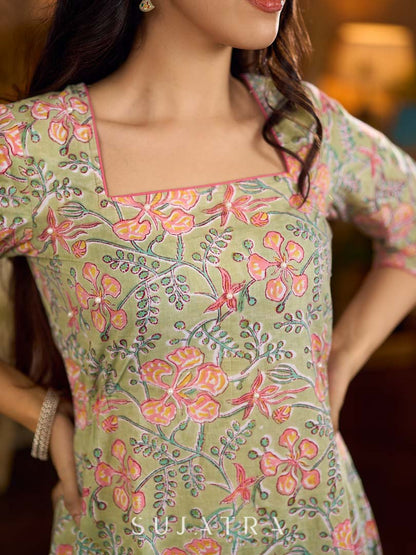 Soft green Gulmohar-printed dress featuring a square neckline and pearl-highlighted motifs, finished with an elasticated waist to create a flattering cinched silhouette with effortless charm.