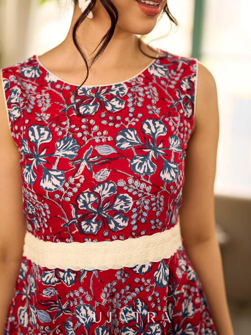 Red Gulmohar floral-printed sleeveless summer dress featuring off-white accents and scalloped lace detailing at the waist, creating a breezy, feminine silhouette perfect for warm, sunlit days.