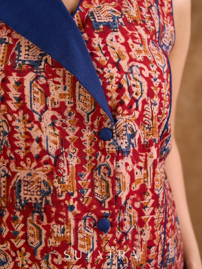 Sharp sleeveless red Kalamkari overlap jacket with a statement one-sided flap, Chinese collar, and navy accents, offering a clean, structured silhouette ideal for elevated corporate styling.