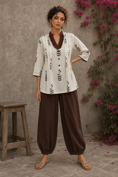 Off-white floral printed top with brown ruffled collar, button front, tie-up sleeves, tassel details, and contrast accents.