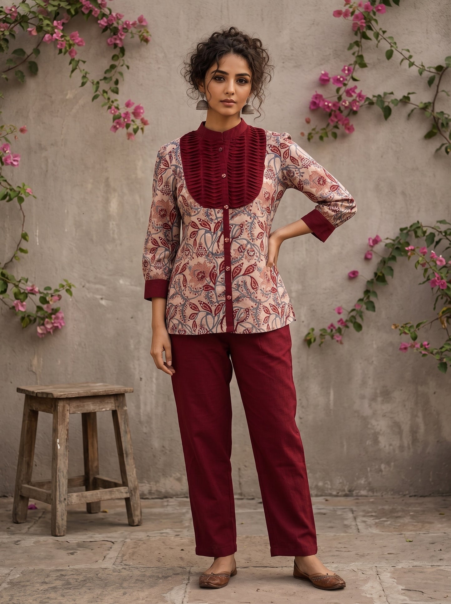 Elegant maroon floral top with intricate maroon pleats, high neckline, covered buttons, and coordinating sleeve cuffs.