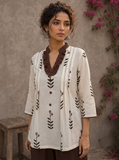 Off-white floral printed top with brown ruffled collar, button front, tie-up sleeves, tassel details, and contrast accents.