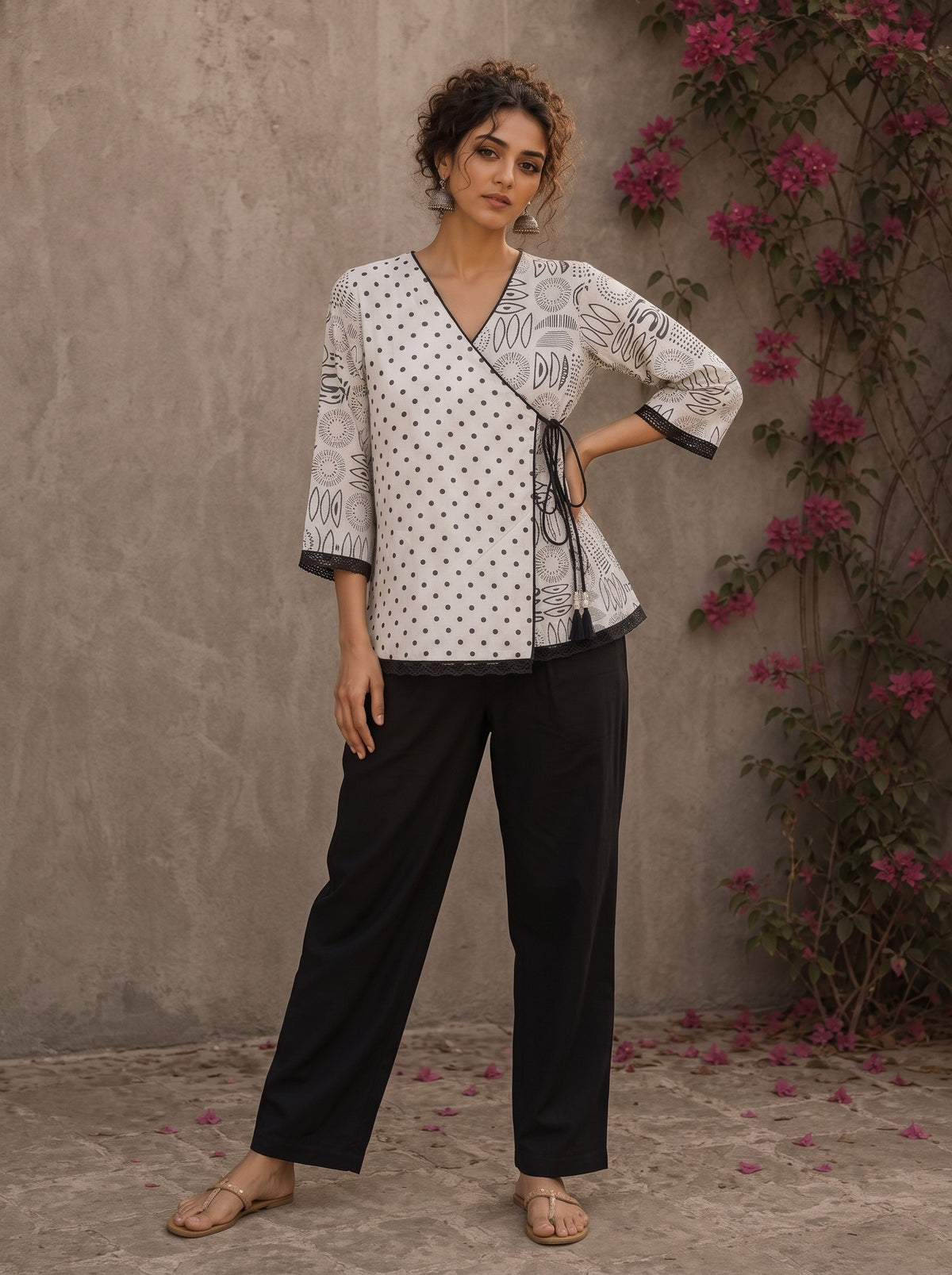 Black and white printed crossover top with contrast polka dots, lace-trimmed sleeves, side tie, tassels, and scalloped hem.