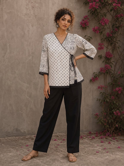Black and white printed crossover top with contrast polka dots, lace-trimmed sleeves, side tie, tassels, and scalloped hem.