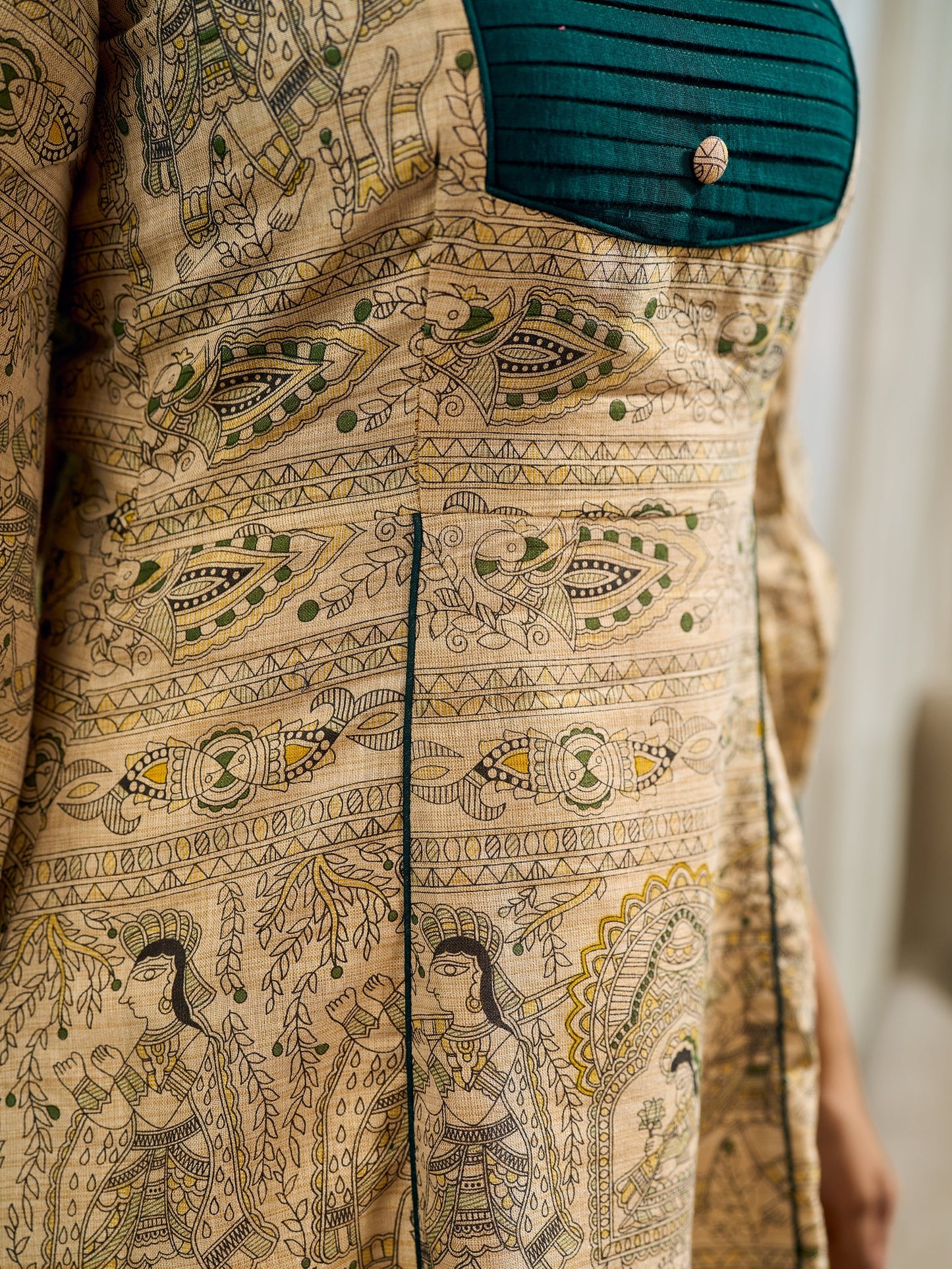 Artisanal beige Madhubani dress featuring intricate motifs, a contrasting green yoke, and refined accents.