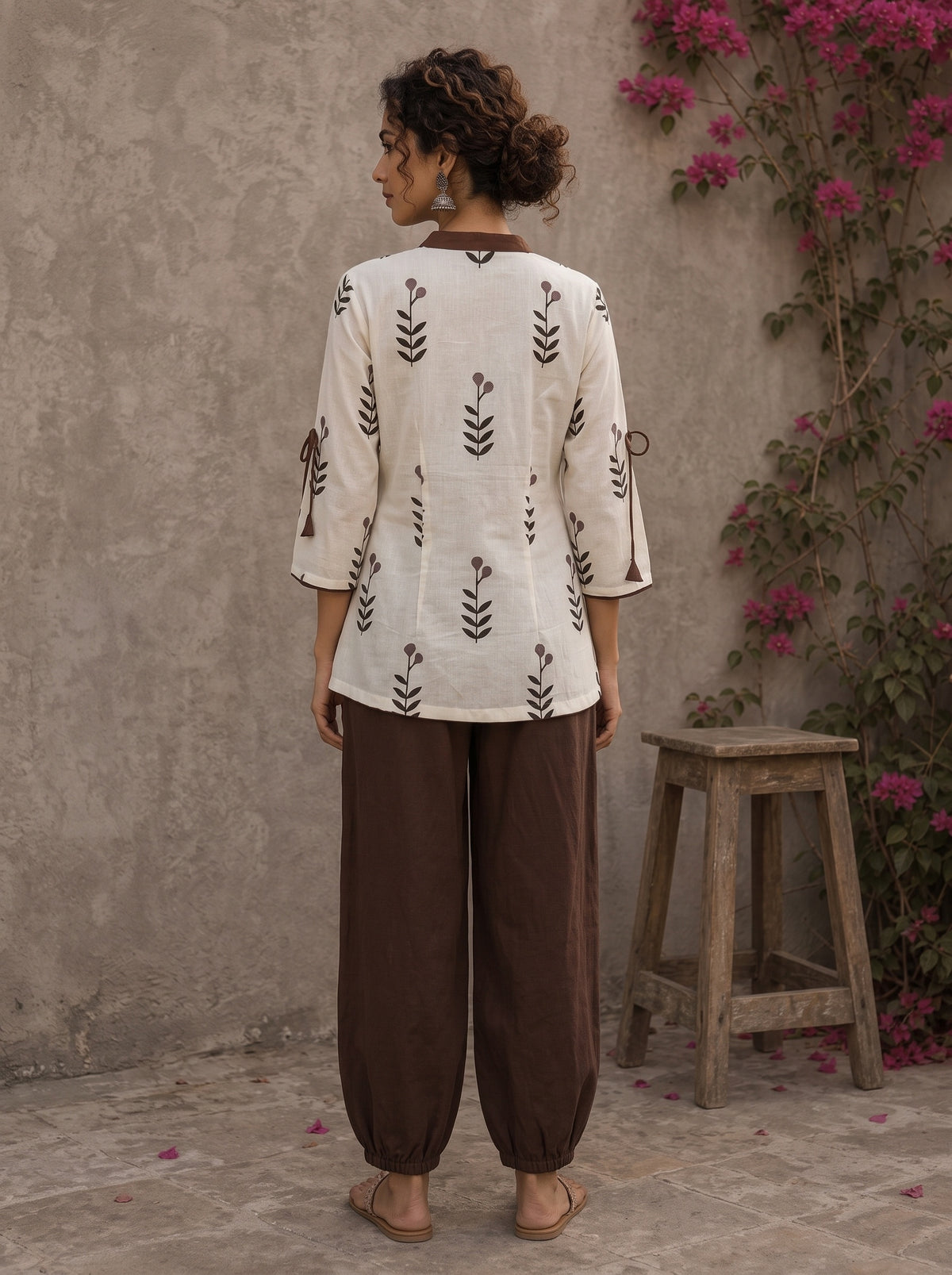 Off-white floral printed top with brown ruffled collar, button front, tie-up sleeves, tassel details, and contrast accents.