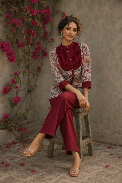 Elegant maroon floral top with intricate maroon pleats, high neckline, covered buttons, and coordinating sleeve cuffs.