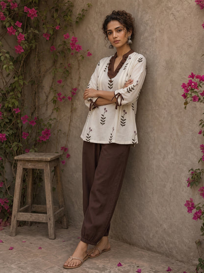 Off-white floral printed top with brown ruffled collar, button front, tie-up sleeves, tassel details, and contrast accents.