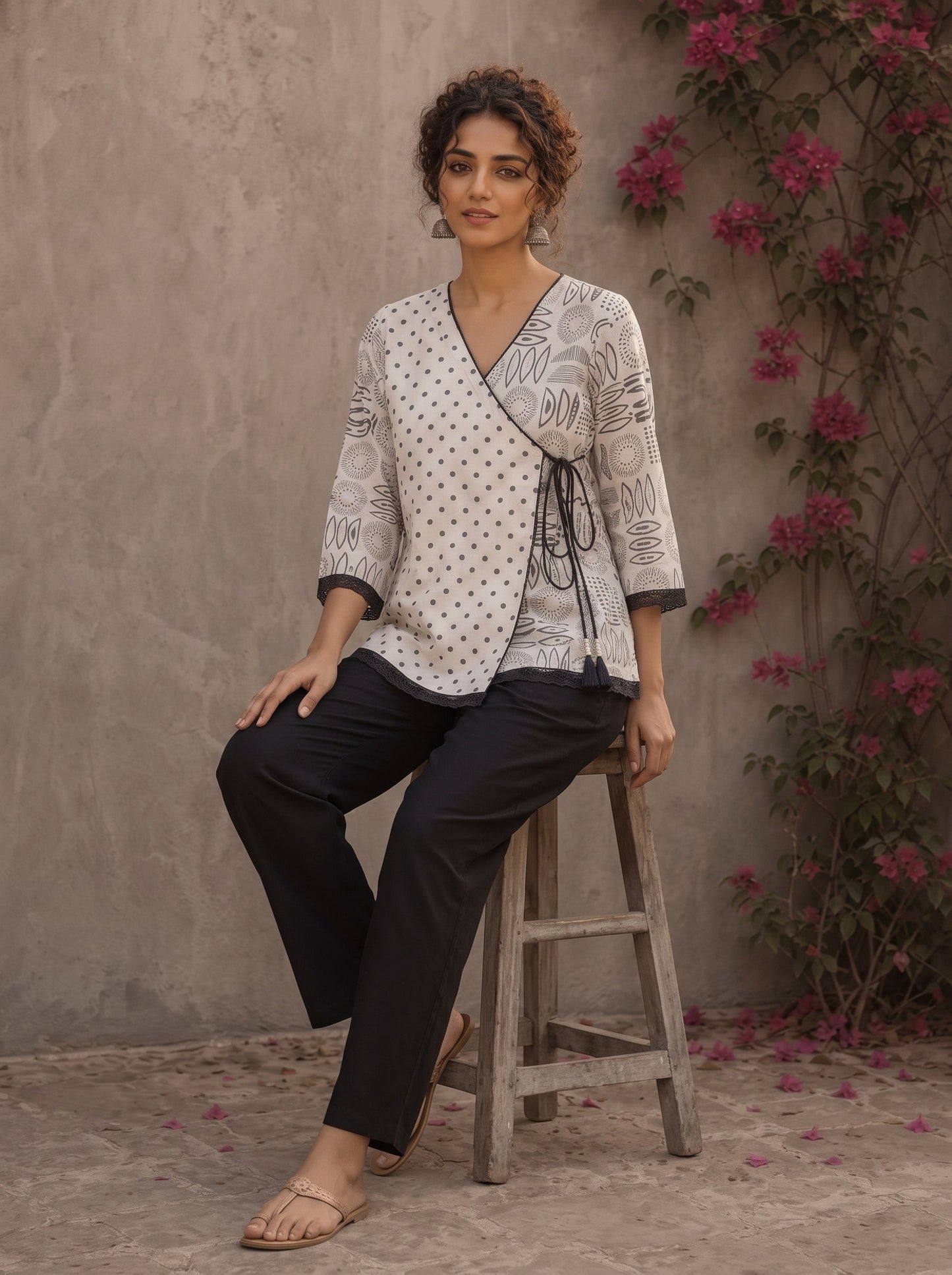 Black and white printed crossover top with contrast polka dots, lace-trimmed sleeves, side tie, tassels, and scalloped hem.