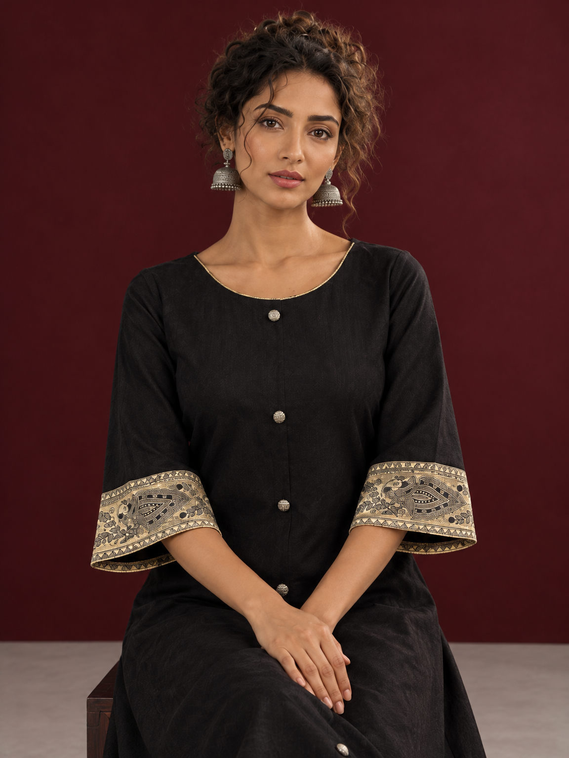Elegant Black Cotton A-Line Dress with Madhubani Print Border Hem and Matching Bell Sleeve Cuffs — seated detail — view 5