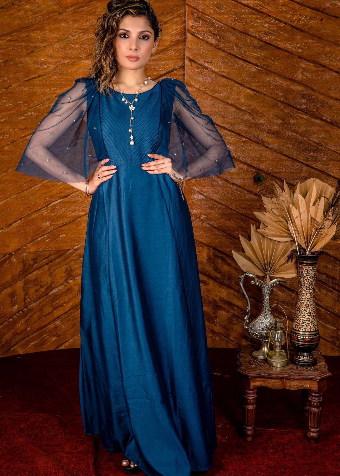 Blue satin gown with net sleeves, sequence work & self tucks on yoke.