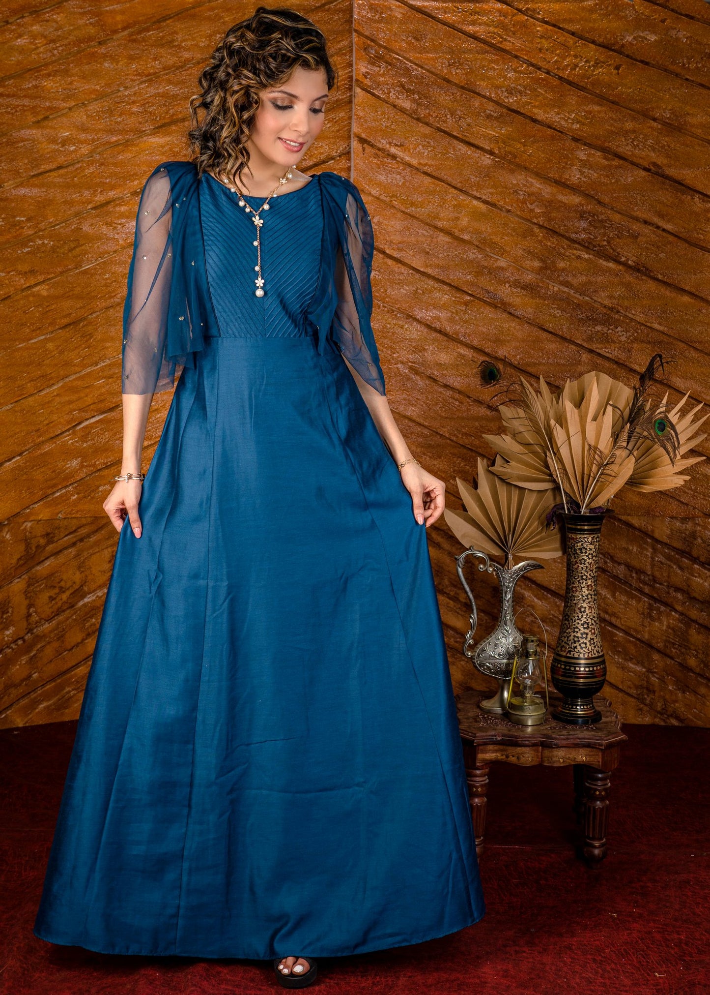 Blue satin gown with net sleeves, sequence work & self tucks on yoke.