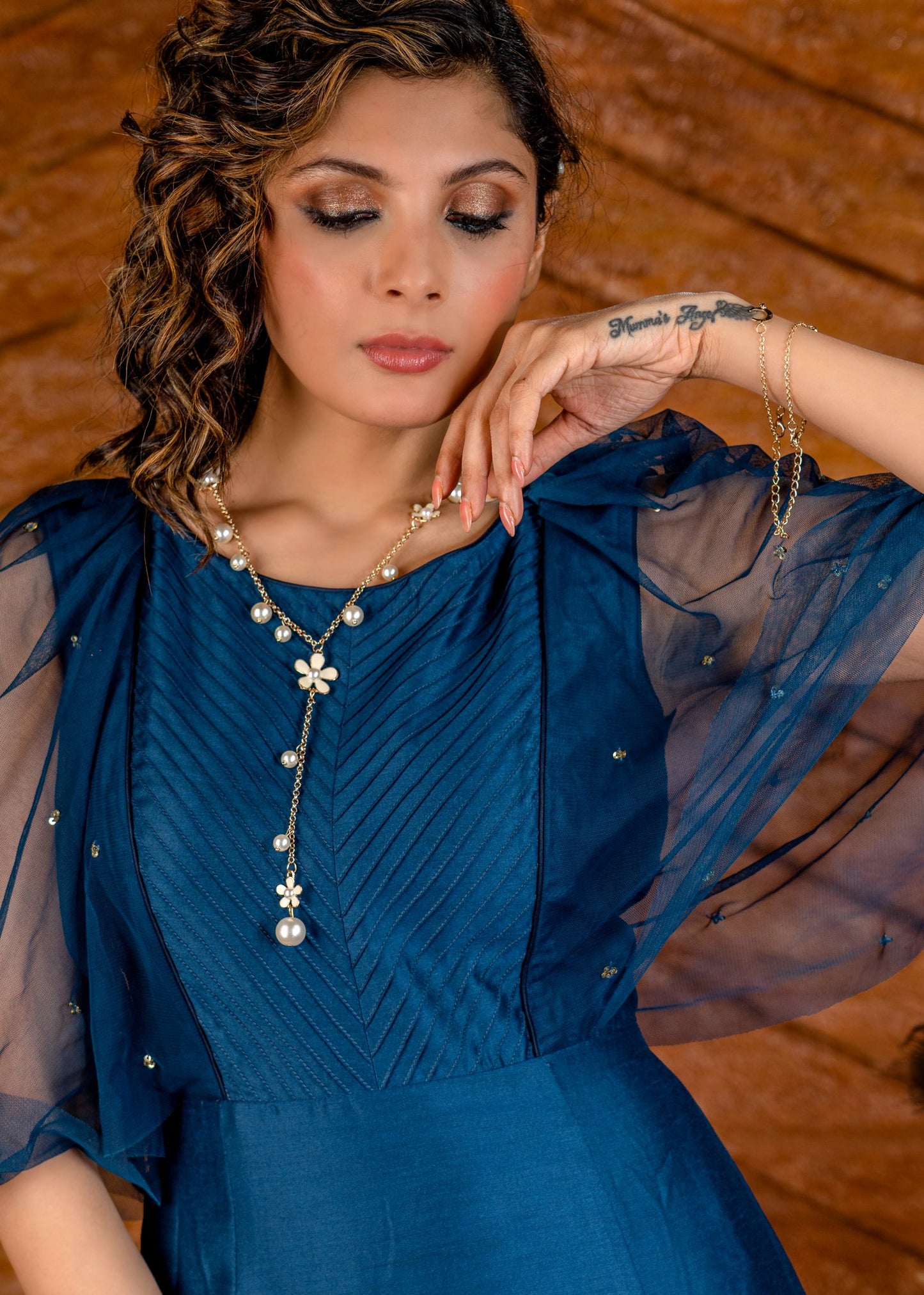 Blue satin gown with net sleeves, sequence work & self tucks on yoke.
